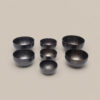 Seven hand-hammered note bowls from the Pure Bliss C4 Healing Bowl Set in a midnight black finish, arranged in varying sizes on a plain background.
