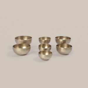 Seven hand-hammered note bowls from the Pure Bliss C4 Healing Bowl Set in a matte gold finish, arranged in varying sizes on a plain background.