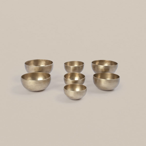 Seven hand-hammered note bowls from the Pure Bliss C4 Healing Bowl Set in a matte gold finish, arranged in varying sizes on a plain background.
